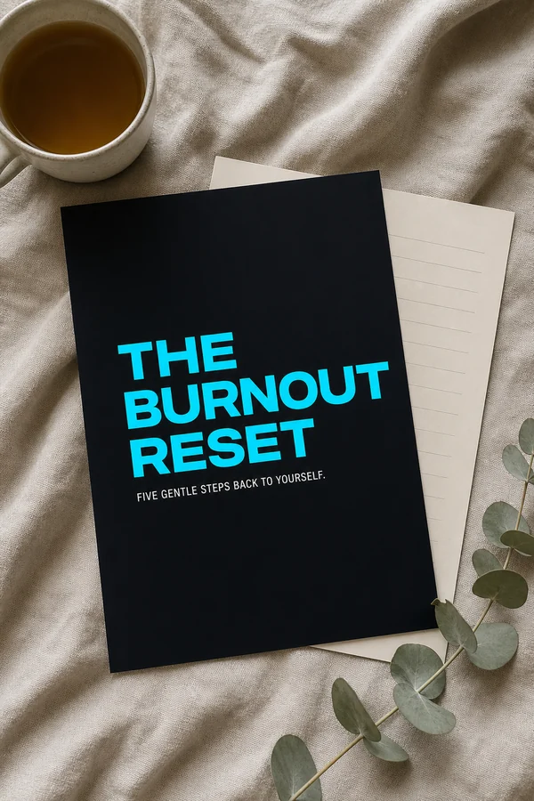 The Burnout Reset printed and lying on a desk in soft morning light beside a mug, with a cream worksheet showing ruled lines.