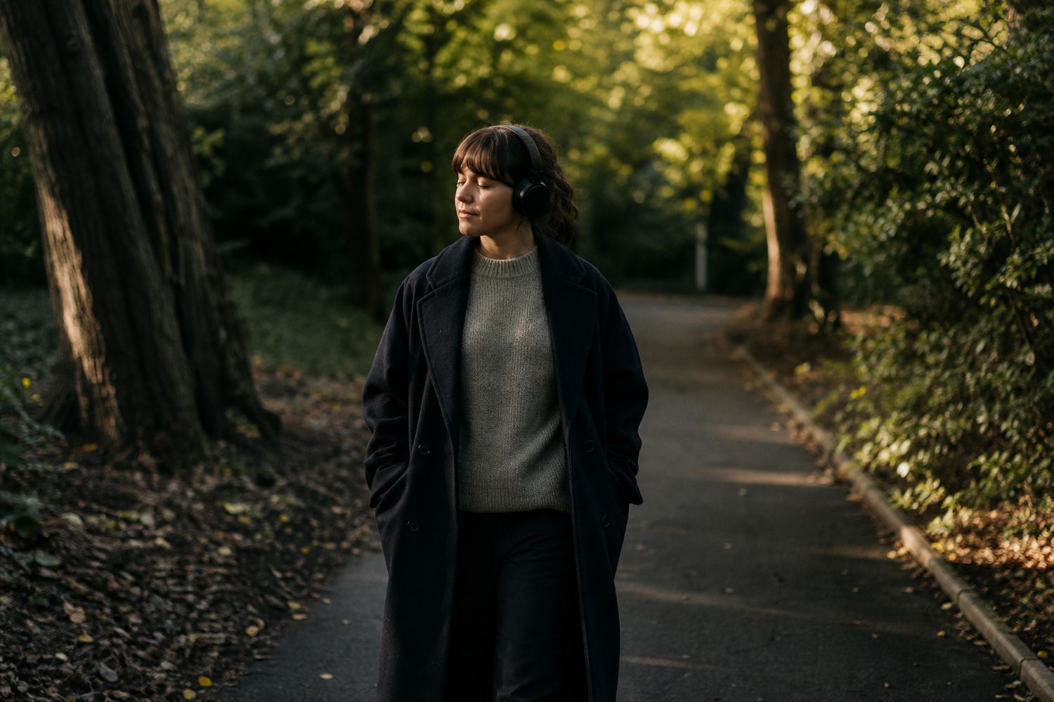 A person walking along a quiet tree lined path in soft afternoon light, relaxed posture, headphones on, taking a deliberate break