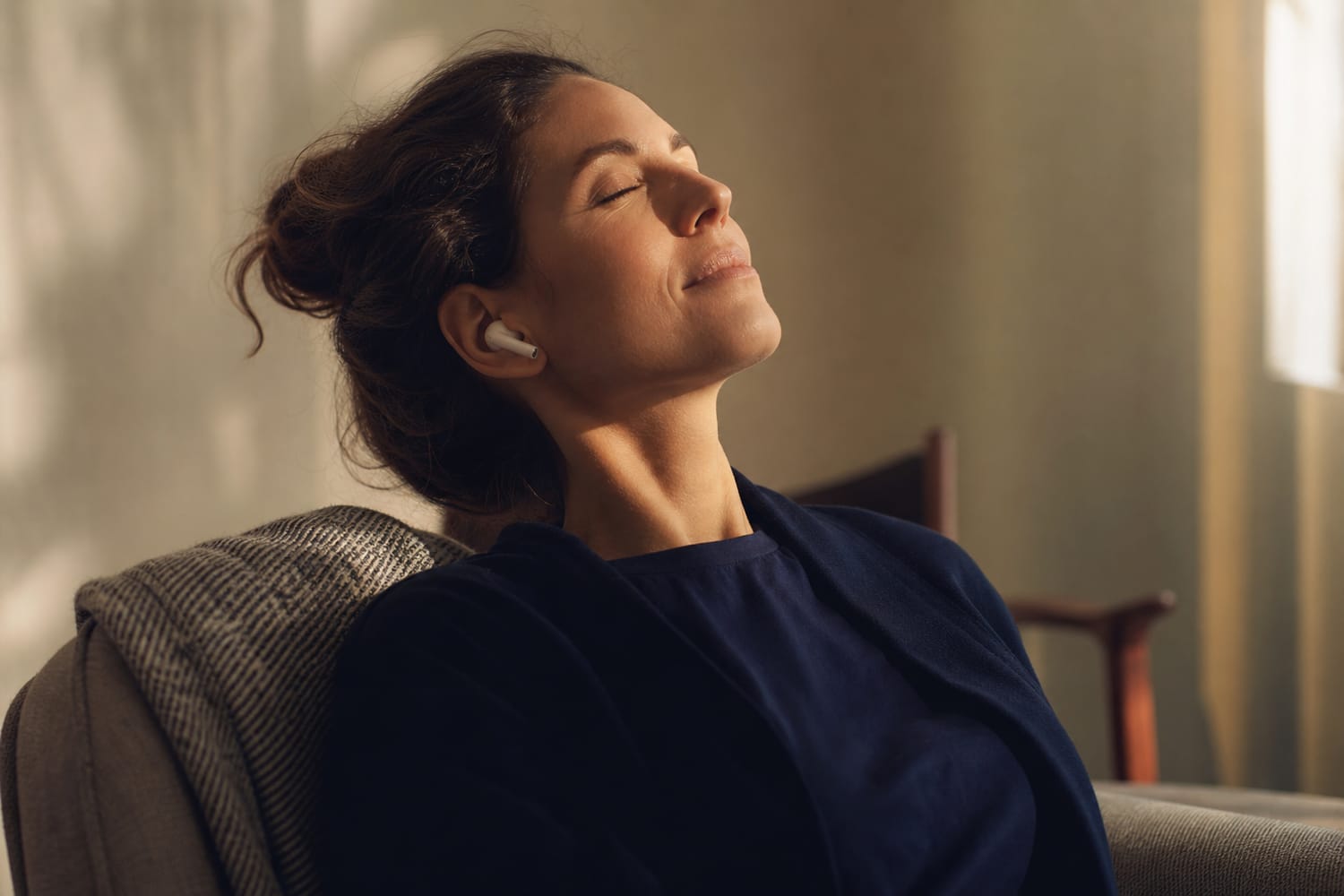 A woman relaxing with eyes closed wearing earbuds, head tilted back.