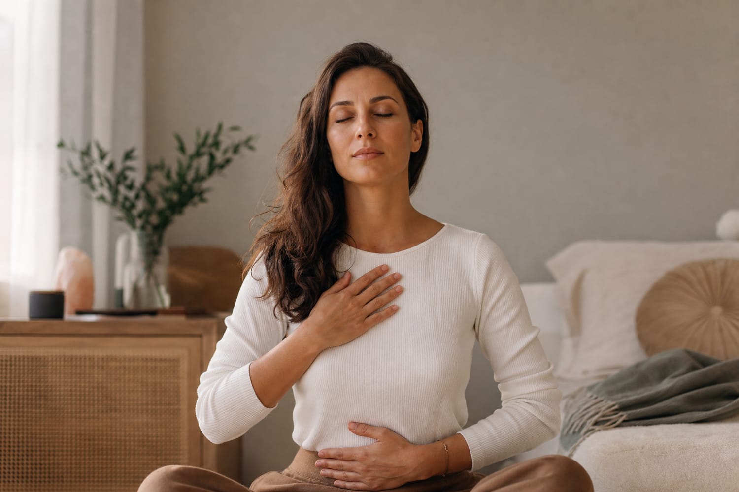 A woman sitting calmly with her eyes closed, taking a slow steadying breath in soft natural light, grounding herself in the present.