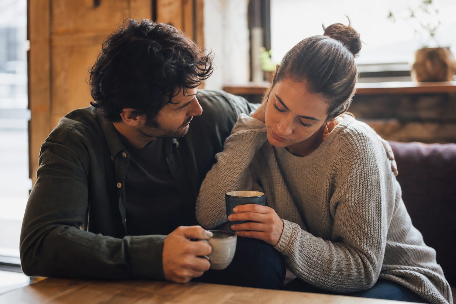 Two friends, a man and a woman, talking supportively over coffee, one leaning on the other in an open, honest conversation, warm natural light.