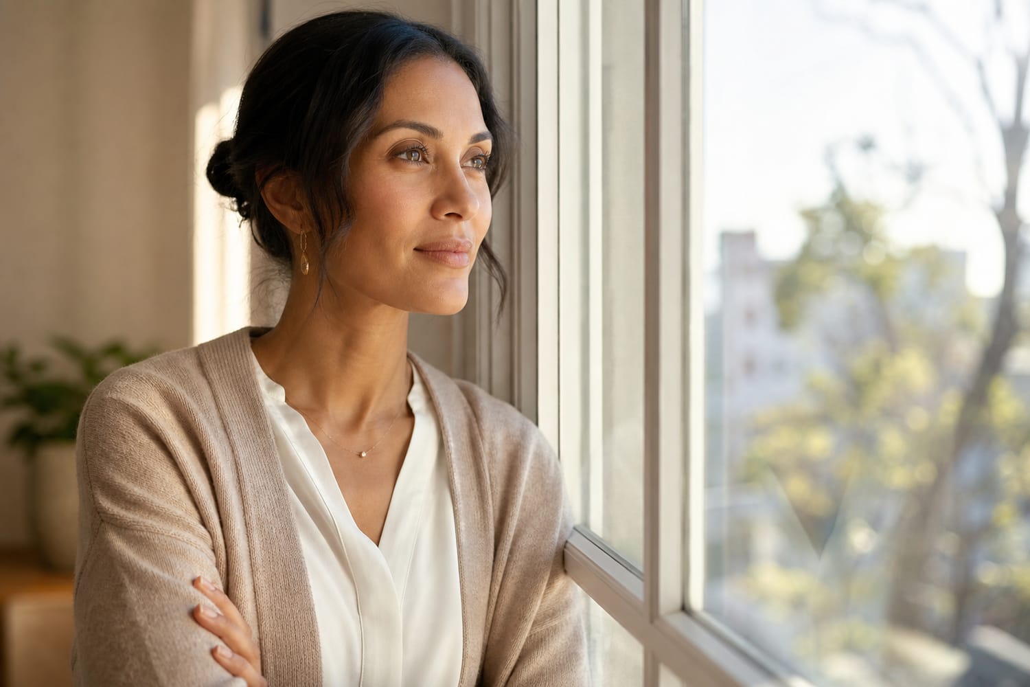 A woman pausing thoughtfully by a window with a calm, quietly confident expression, choosing a kinder inner response, soft morning light.